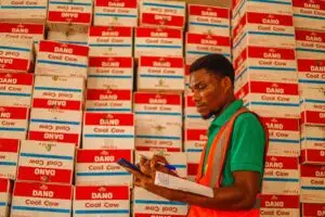 Focused warehouse employee taking inventory notes amid stacks of Dano Cool Cow boxes.